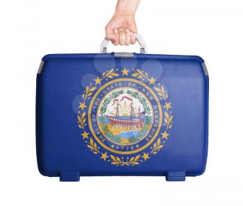Used plastic suitcase with stains and scratches, printed with flag, New Hampshire