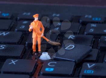 Miniature worker with broom working on a computer keyboard
