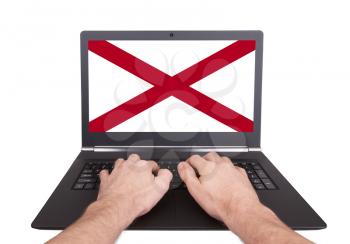 Hands working on laptop showing on the screen the flag of Alabama