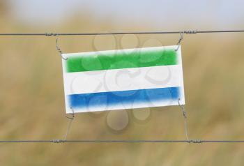 Border fence - Old plastic sign with a flag - Sierra Leone