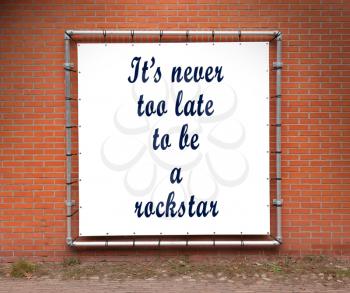 Large banner with inspirational quote on a brick wall - It's never too late to be a rockstar
