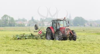 Farmer uses tractor to spread hay on the field where it will dry