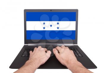Hands working on laptop showing on the screen the flag of Honduras