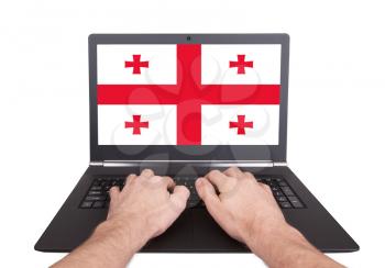 Hands working on laptop showing on the screen the flag of Georgia