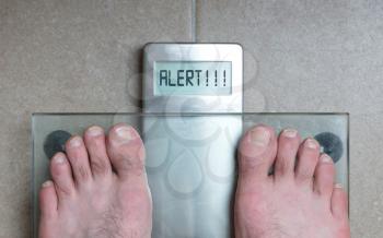 Closeup of man's feet on weight scale - Alert