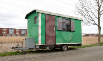Old green wooden trailer on wheels stands at the side of the road, the Netherlands