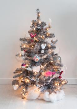 Isolated decorated christmas tree, silver tree with a white wall