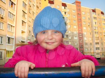 The blue-eyed girl on a horizontal bar on a background of the multi-storey house