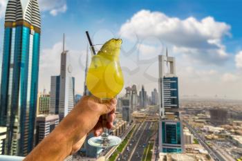 Hand holds glass with fresh pineapple juice over Dubai in a summer day, United Arab Emirates