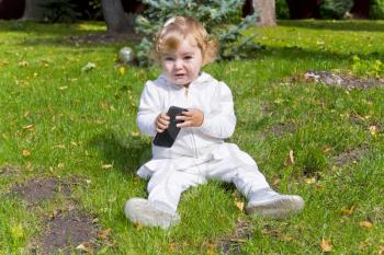 Cute baby girl with mobile phone sitting on green grass