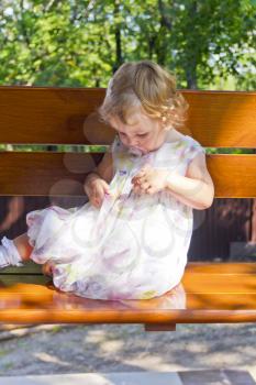 Baby girl with curly hair sitting on bench in sunlight