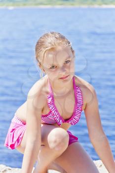 Cute angry girl on the riverbank in pink swimsuit