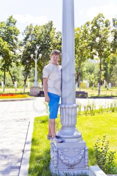 Blond boy near pole in blue trousers playing summer time