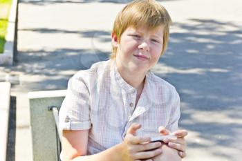 Blond boy with mobile phone sitting on a bench