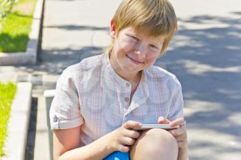 Blonde smiling boy with cellular phone in summer
