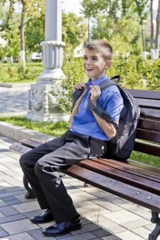 Brunette boy are sitting on the bench with school backpack