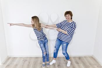 Happiest mother and daughter playing near white wall in striped clothes