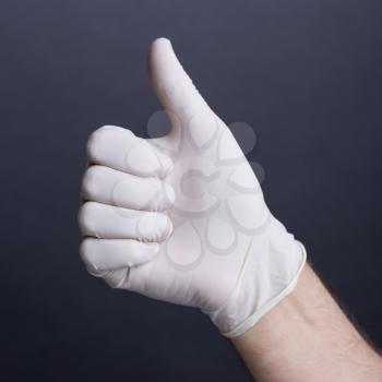 Male hand in latex glove (thumb up sign) on dark background