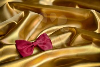 Red bow tie on draped golden satin