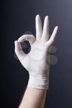 Male hand in latex glove OK sign on dark background