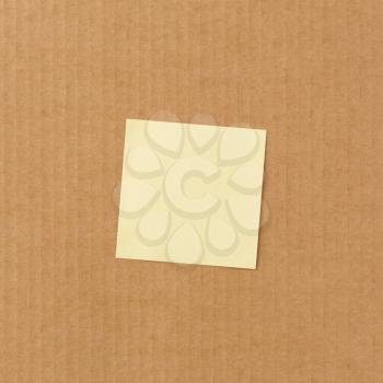 Yellow sticky paper note on corrugated cardboard background