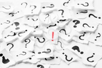 Pile of question mark signs scattered around with one red exclamation symbol in the center. Decision, enquiry or faq concept.