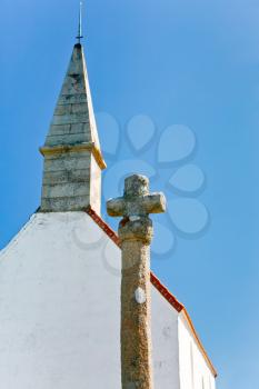 old stone cross and roof of country Chapelle Saint Michel with blue sky background