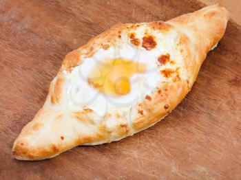 Ajarian khachapuri (Georgian cheese pastry), filled with cheese and topped with a soft-boiled egg and butter on wooden board