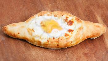 top view of hachapuri by Adzharia (Georgian cheese pastry) , filled with cheese and topped with a soft-boiled egg and butter on wooden board