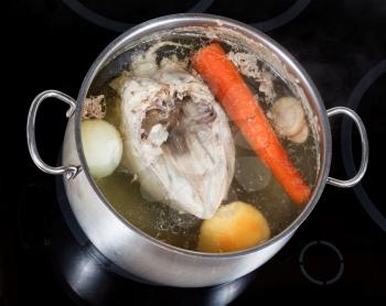 boiling of chicken broth with seasoning vegetables in steel pan on glass ceramic cooker