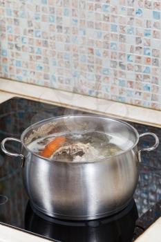 simmering chicken broth with seasoning vegetables in steel pot on glass ceramic cooker