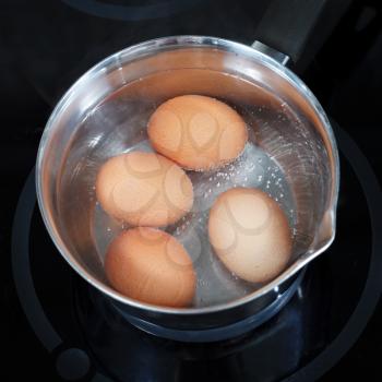 top view of boiling chicken eggs in metal pot on electric stove in kitchen