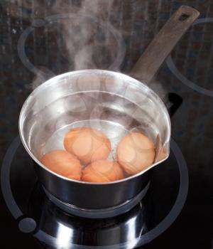 boiling chicken eggs in metal pot on electric stove in kitchen