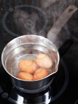simmering chicken eggs in metal pot on electric stove in kitchen