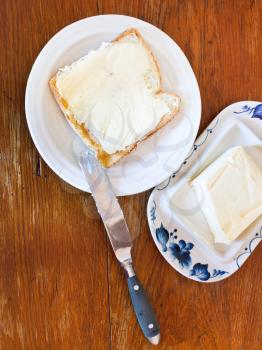 bread and butter sandwich on white plate, knife, dairy butter, butterdish on wooden table