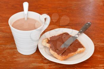 cup of hot chocolate and sweet sandwich from fresh toast with chocolate spread, table knife on wooden table