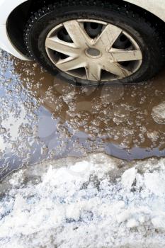poor road condotions - car wheel in melting show puddle