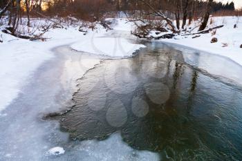 frozen riverbank of forest stream at winter sunset