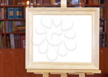 white canvas of wide wood picture frame on easel with clipping path and home library on background