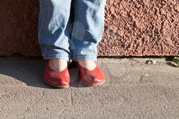 legs in blue jeans and red shoes near wall in autumn day
