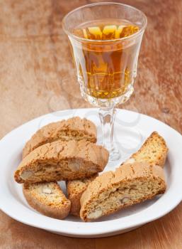 crystal glass with white wine and italian almond cantuccini on saucer on wooden table