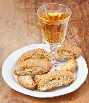 crystal glass with sweet white wine and italian almond cantuccini on saucer on wooden table