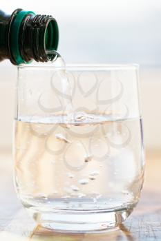mineral water pouring into glass from green bottle