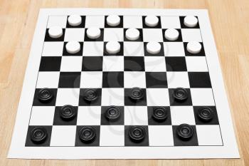 Starting position on vinyl 8x8 draughts board on wooden table