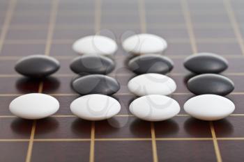 position of stones during go game playing on wooden board close up