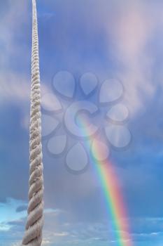 thick rope rises in blue sky with rainbow