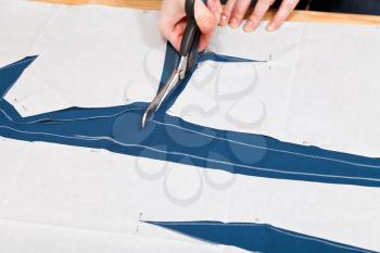 fitter cuts out clothes from blue fabric according with pattern