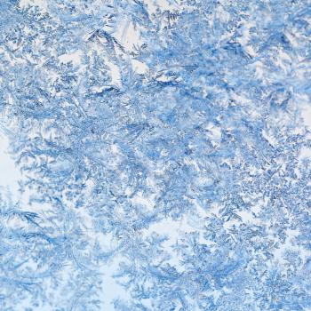 snowflakes and frost on glass close up - frosty blue pattern on window in cold winter day