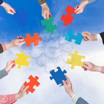 circle of people hands with different puzzle pieces with blue sky and white cloud background