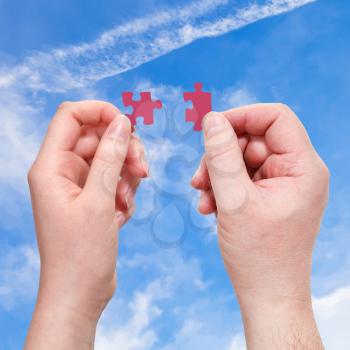 male and female hands with red puzzle pieces with blue sky background
